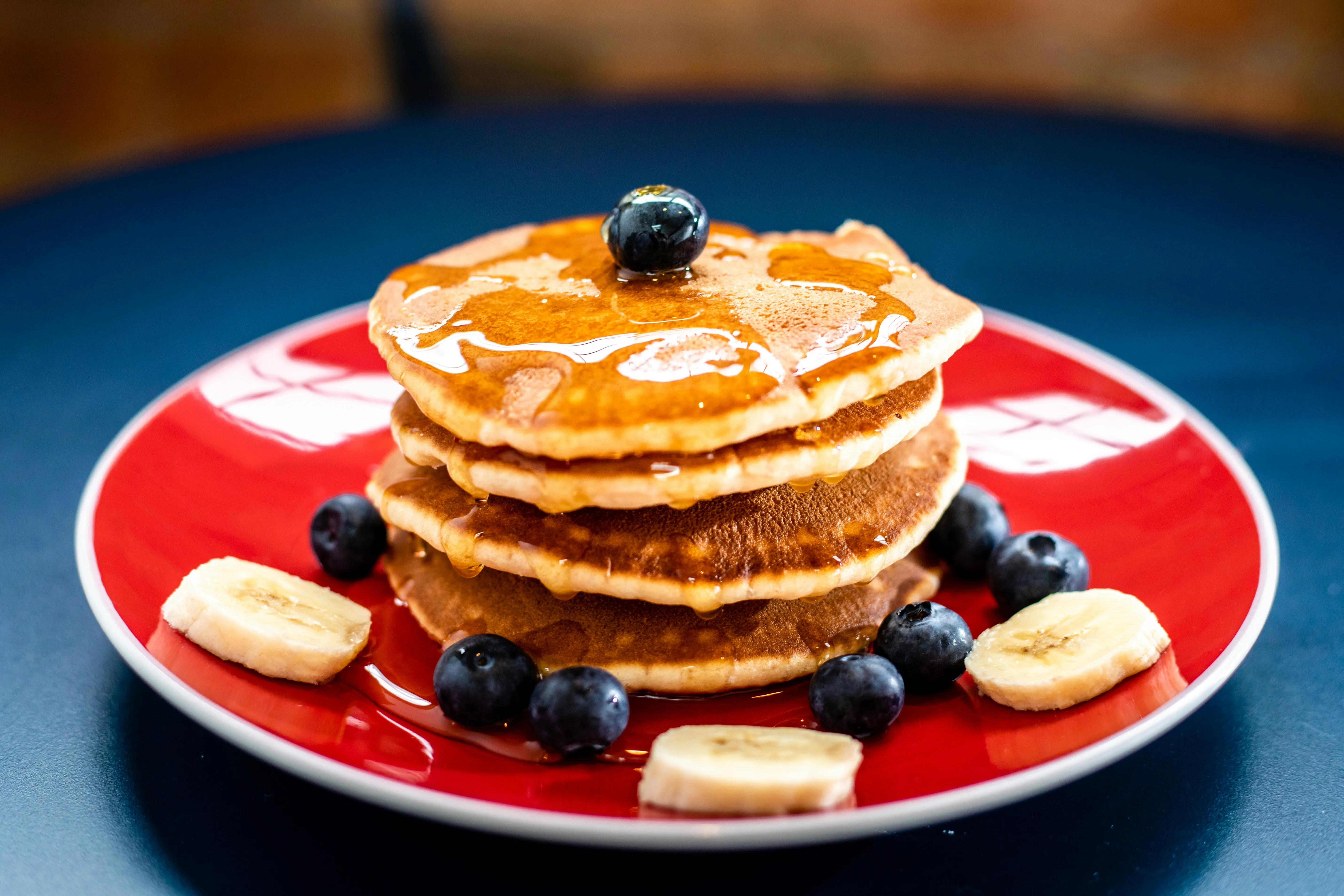 A stack of pancakes with syrup, blueberries and bananas.